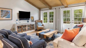 Una sala de estar con televisor, asientos, una mesa de centro y vistas amplias a través de grandes ventanales.