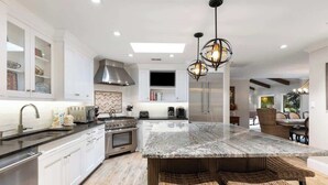 Una cocina moderna con armarios blancos, una isla de mármol y una estufa integrada.