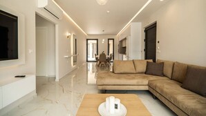 A modern living room with a beige sofa, a wooden coffee table, and a flat-screen TV mounted on the wall. - Elixir Villa 7BD 4BD 14PL - 3min walk to the beach (Georgioupoli)