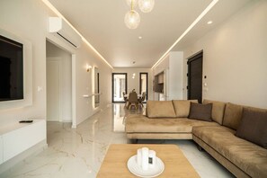 Ein modernes Wohnzimmer mit einem beigen Sofa, einem Couchtisch aus Holz und einem an der Wand montierten Flachbildfernseher.