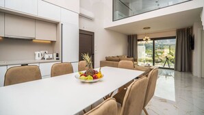 A modern kitchen with white cabinets, a dining table with chairs, and a fruit bowl. - Elixir Villa 7BD 4BD 14PL - 3min walk to the beach (Georgioupoli)