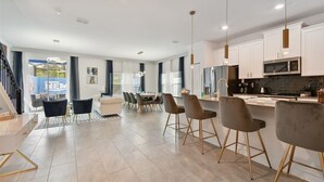 A modern kitchen with white cabinets, a microwave, and a sink. There is a dining area with a table and chairs. - 5BR Storey Lake Home, Heated Pool (kissimmee)