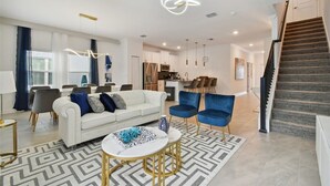 A modern living room with a white sofa, blue chairs, a coffee table, and a staircase leading to the upper floor. - 5BR Storey Lake Home, Heated Pool (kissimmee)
