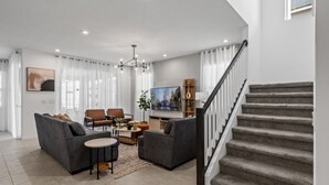 A modern living room with a sofa set, a coffee table, and a TV. There is a staircase with a railing leading to an upper floor. - 6BR/5BA Luxurious with Private Pool (Kissimmee)