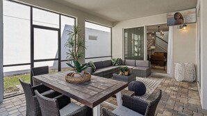 An outdoor patio with a wooden table, wicker chairs, and a seating area with cushions. - 6BR/5BA Luxurious with Private Pool (Kissimmee)
