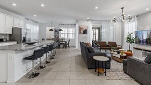 A modern kitchen with a central island, bar stools, and a dining area with chairs and a table. - 6BR/5BA Luxurious with Private Pool (Kissimmee)