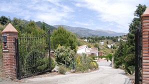 A gated entrance to a residential area with a paved driveway leading to houses. - Villa Los Almendros (Canillas de Albaida)