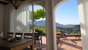 A dining area with a table and chairs, a hanging light fixture, and a view of a mountainous landscape through an arched doorway. - Villa Los Almendros (Canillas de Albaida)