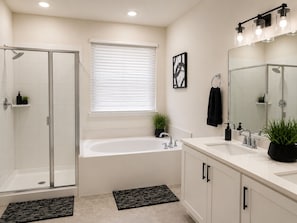 A modern bathroom with a glass shower enclosure, a freestanding bathtub, a large mirror, and a white vanity.