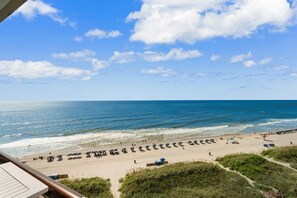 A beach with rows of umbrellas and sun loungers, a clear blue sky, and the ocean.