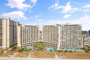 A high-rise hotel with multiple balconies, a central courtyard, and a swimming pool area. - Cozy Oceanview at Beach Cove (North Myrtle Beach)