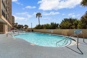 A swimming pool with a lifeguard sign, poolside chairs, and a palm tree in the background. - Cozy Oceanview at Beach Cove (North Myrtle Beach)