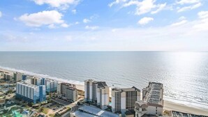 A coastal cityscape with high-rise buildings, a beach, and a clear sky.