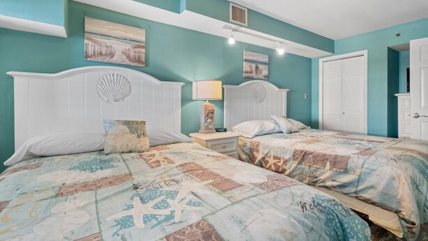 A bedroom with two beds, a nightstand with a lamp, and a door.