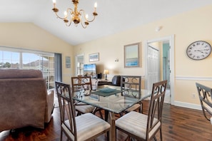 A dining area with a glass table and chairs, a chandelier, and a clock on the wall.