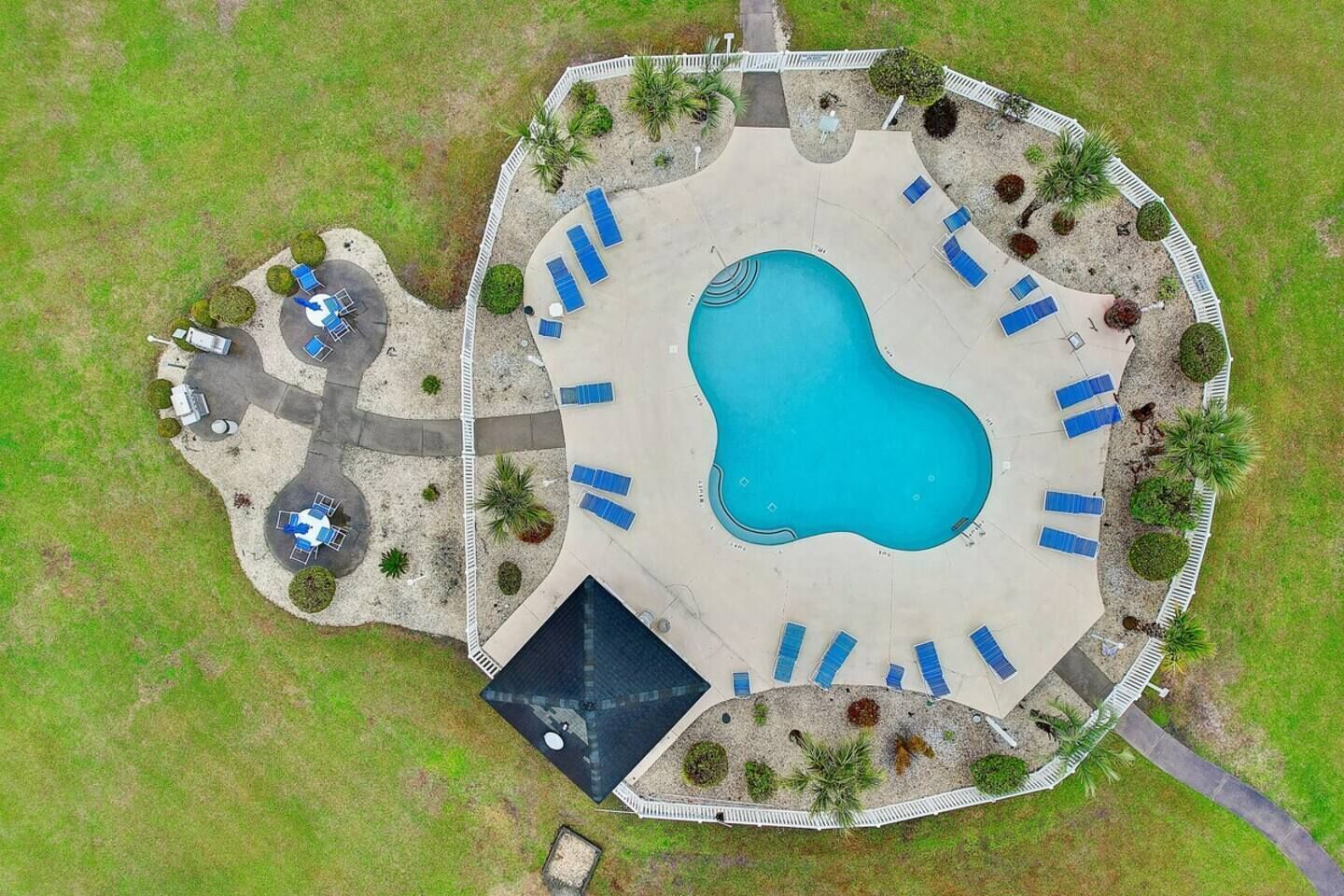 An aerial view of a pool area with a central pool, surrounding lounge chairs, and a fenced perimeter.