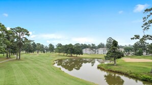 Um campo de golfe com lago, árvores e um edifício ao fundo.