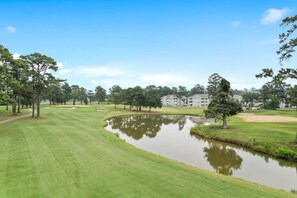 A golf course with a pond, trees, and a building in the background.