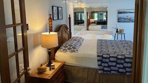 Un dormitorio con cama, mesita de noche, lámpara, espejo y ventilador de techo.