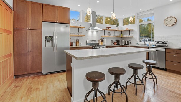 A modern kitchen with wooden cabinets, a stainless steel refrigerator, a central island with stools, and pendant lighting. - Creekside 3BR Retreat Near Downtown, Airport & Fish Creek (Anchorage)