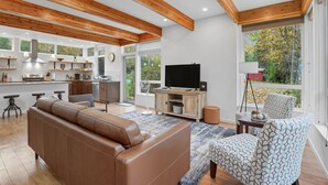A modern living room with a brown leather sofa, a patterned armchair, and a television on a wooden stand. - Creekside 3BR Retreat Near Downtown, Airport & Fish Creek (Anchorage)