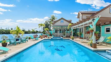 A swimming pool with lounge chairs and potted plants, surrounded by a building with a porch and a view of the water.