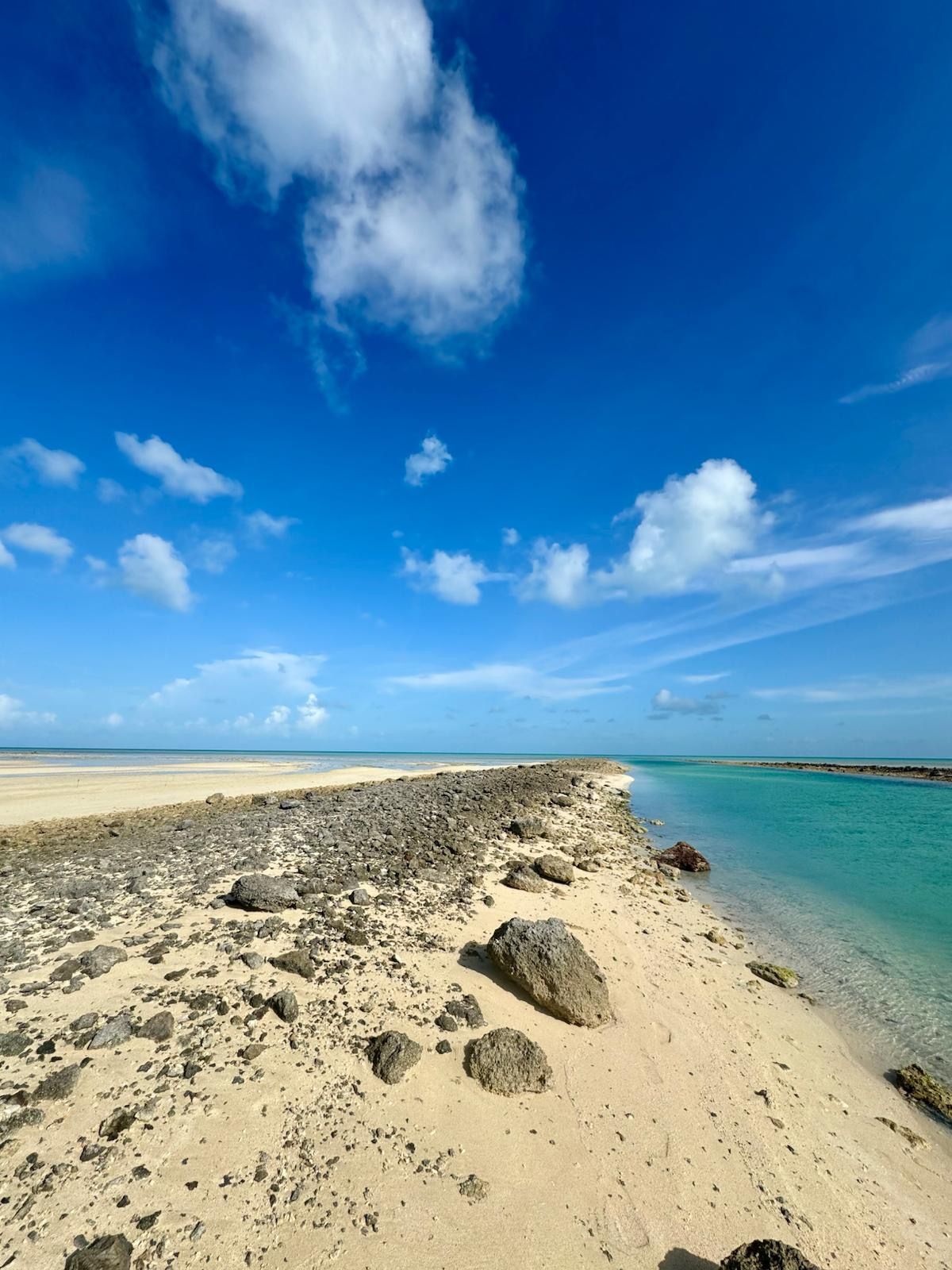 A beach with clear turquoise water, a rocky shoreline, and a clear blue sky.