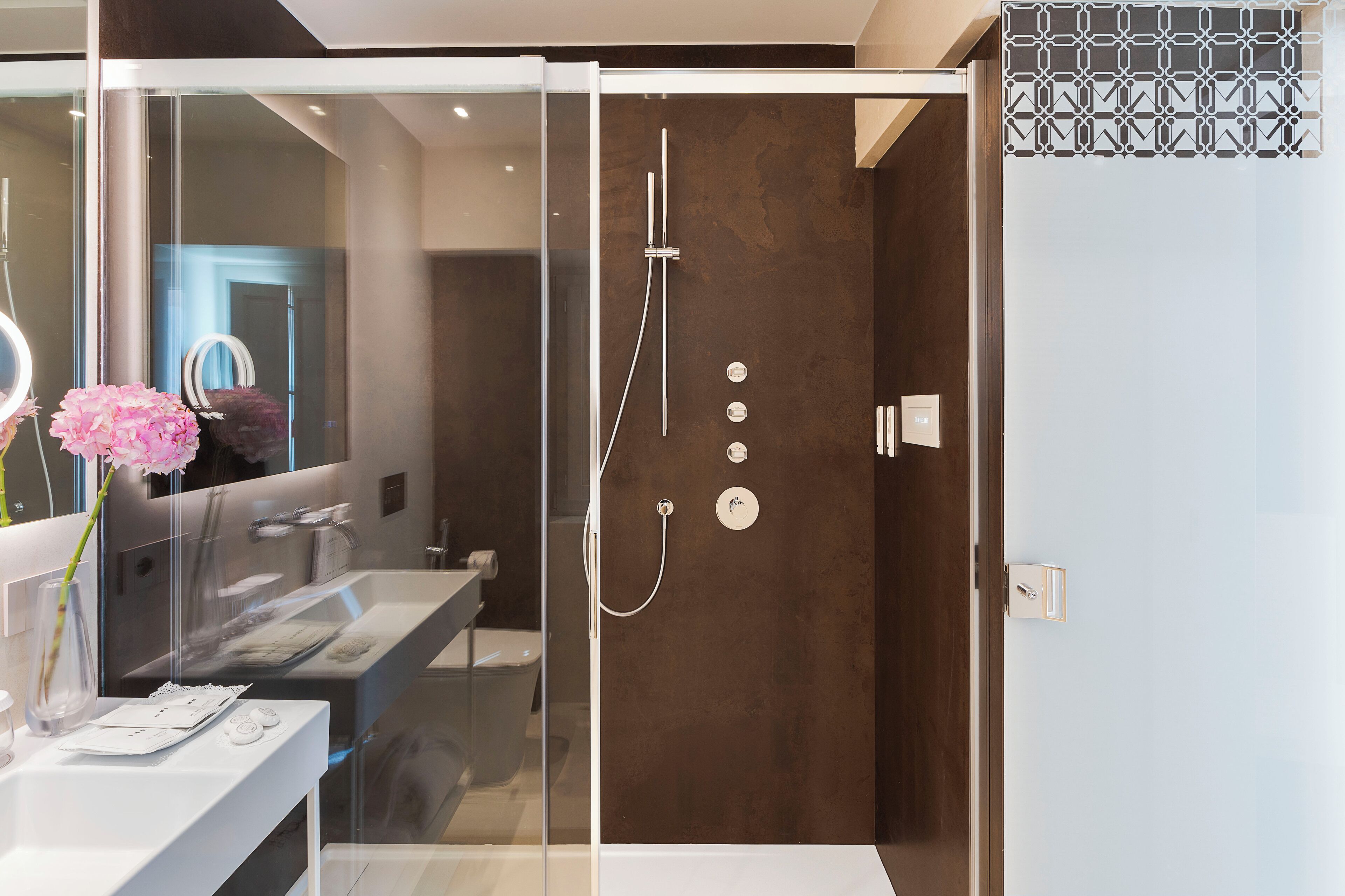 Un baño moderno con ducha acristalada, un espejo grande y un tocador blanco.