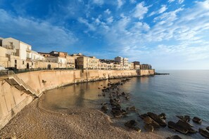 A coastal town with buildings along the waterfront, a pebbled beach, and a clear sky. - Maniace Boutique Hotel Ortigia UNA Esperienze (Syracuse)