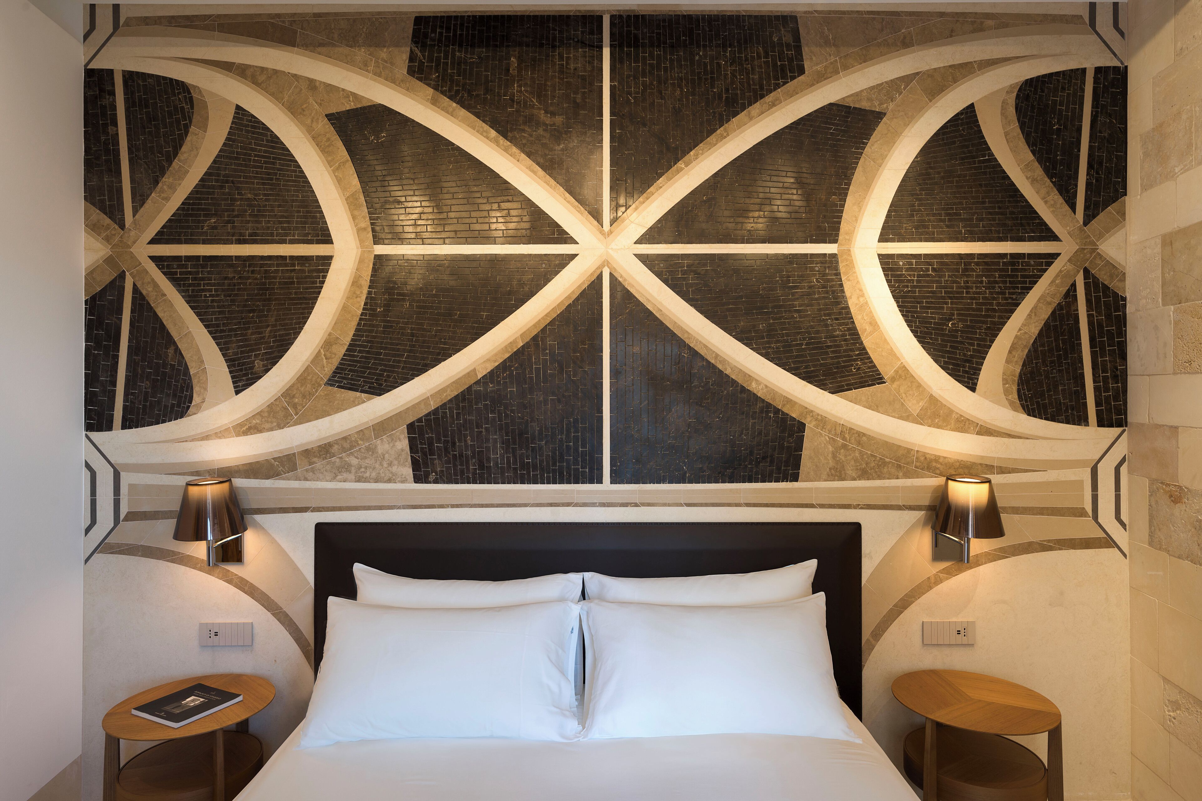 Una habitación de hotel con una cama grande, dos mesitas de noche y una pared decorativa con patrones geométricos.