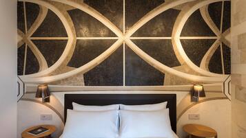 Una habitación de hotel con una cama grande, dos mesitas de noche y una pared decorativa con patrones geométricos.