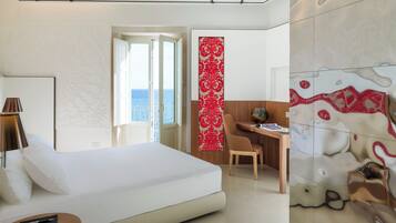 A modern hotel room with a large bed, a desk, and a view of the sea.