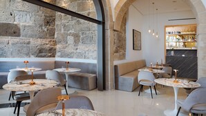 A modern interior with stone walls, round tables, and cushioned seating areas. - Maniace Boutique Hotel Ortigia UNA Esperienze (Syracuse)