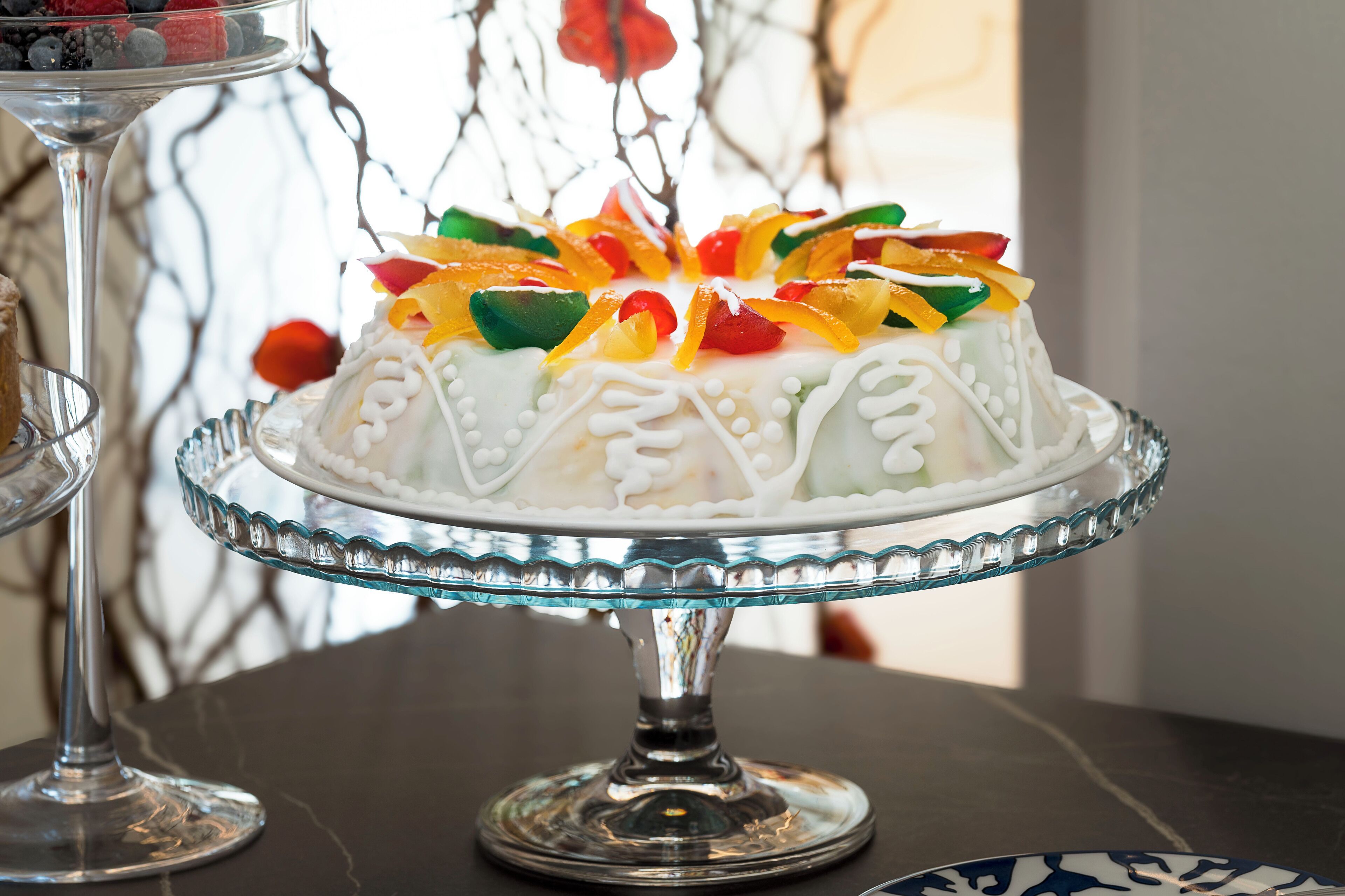 A white cake with colorful decorations on a glass cake stand.