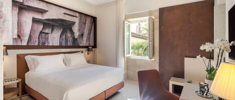 A modern hotel room with a large bed, a desk with a lamp, a chair, and a large abstract painting on the wall.