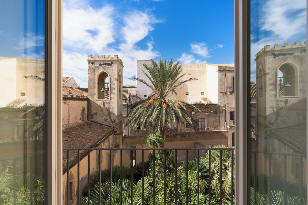 A courtyard with a palm tree, a tower, and buildings with arched windows and balconies.