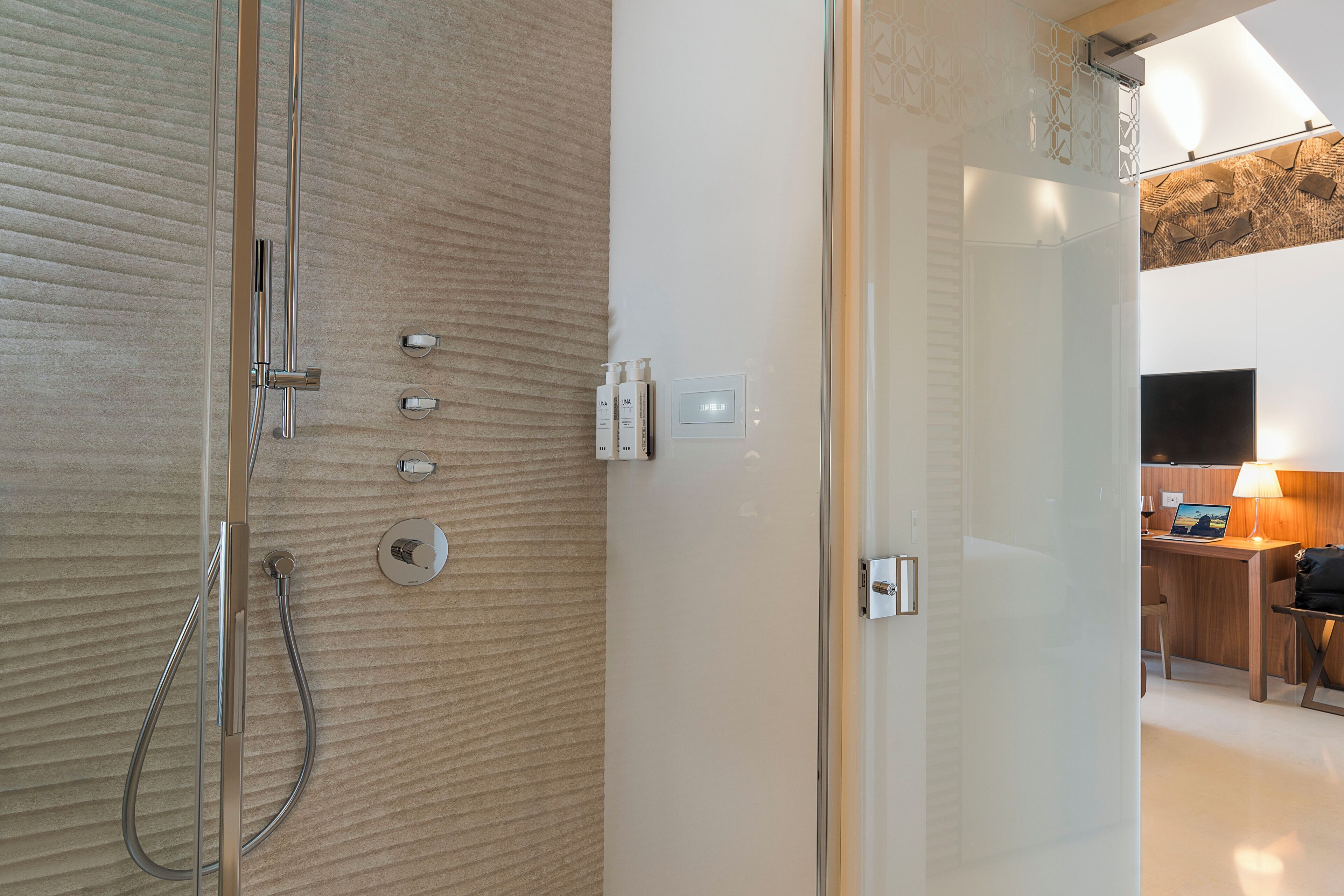 Un baño moderno con cabina de ducha de vidrio, pared con textura de madera y panel de control visible.