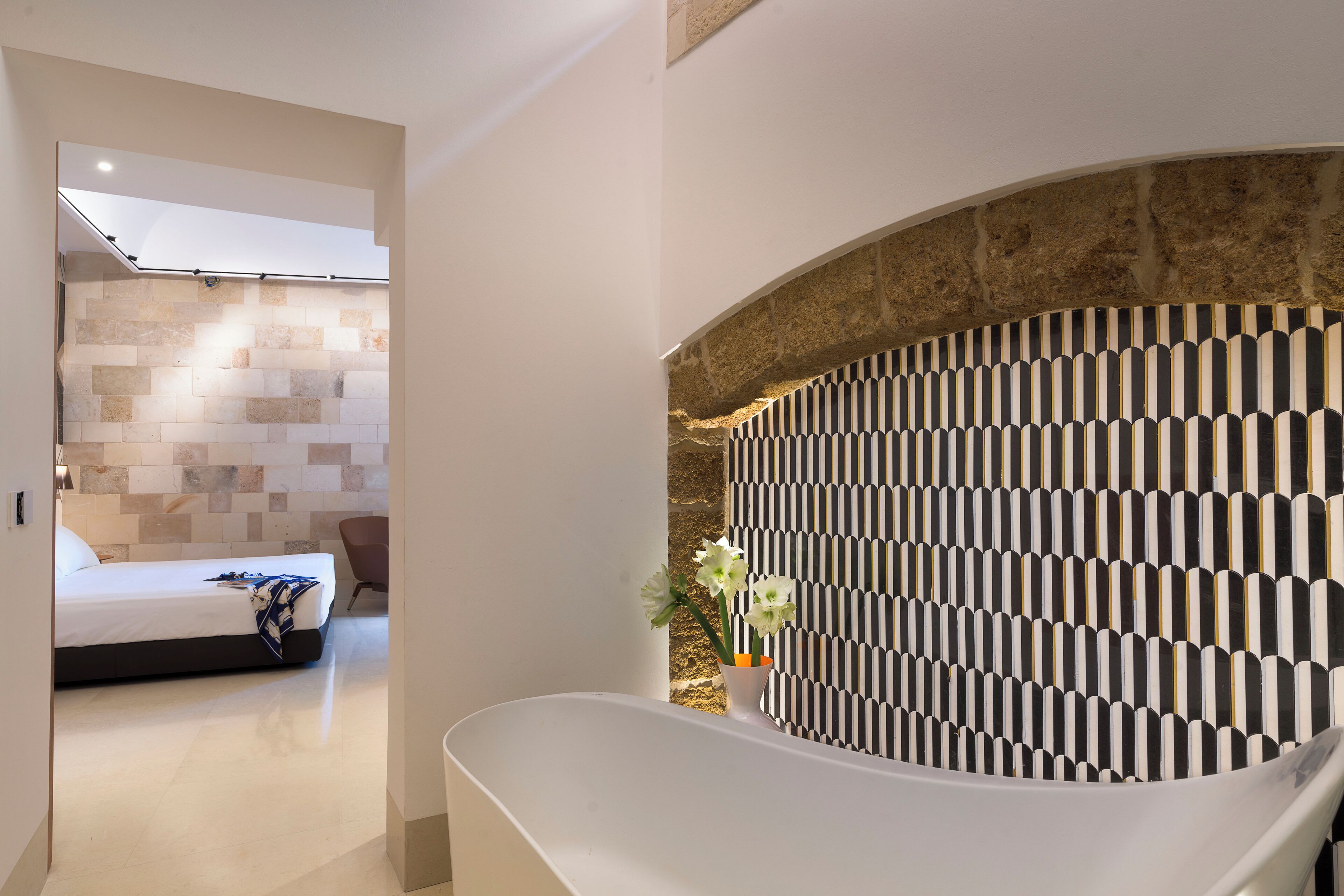 Une salle de bain moderne avec une baignoire sur pieds, un mur en pierre et un mur orné d’un motif.
