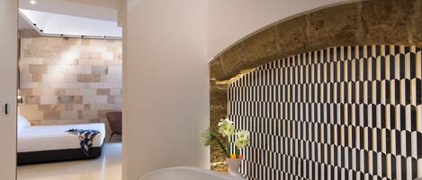 Une salle de bain moderne avec une baignoire sur pieds, un mur en pierre et un mur orné d’un motif.