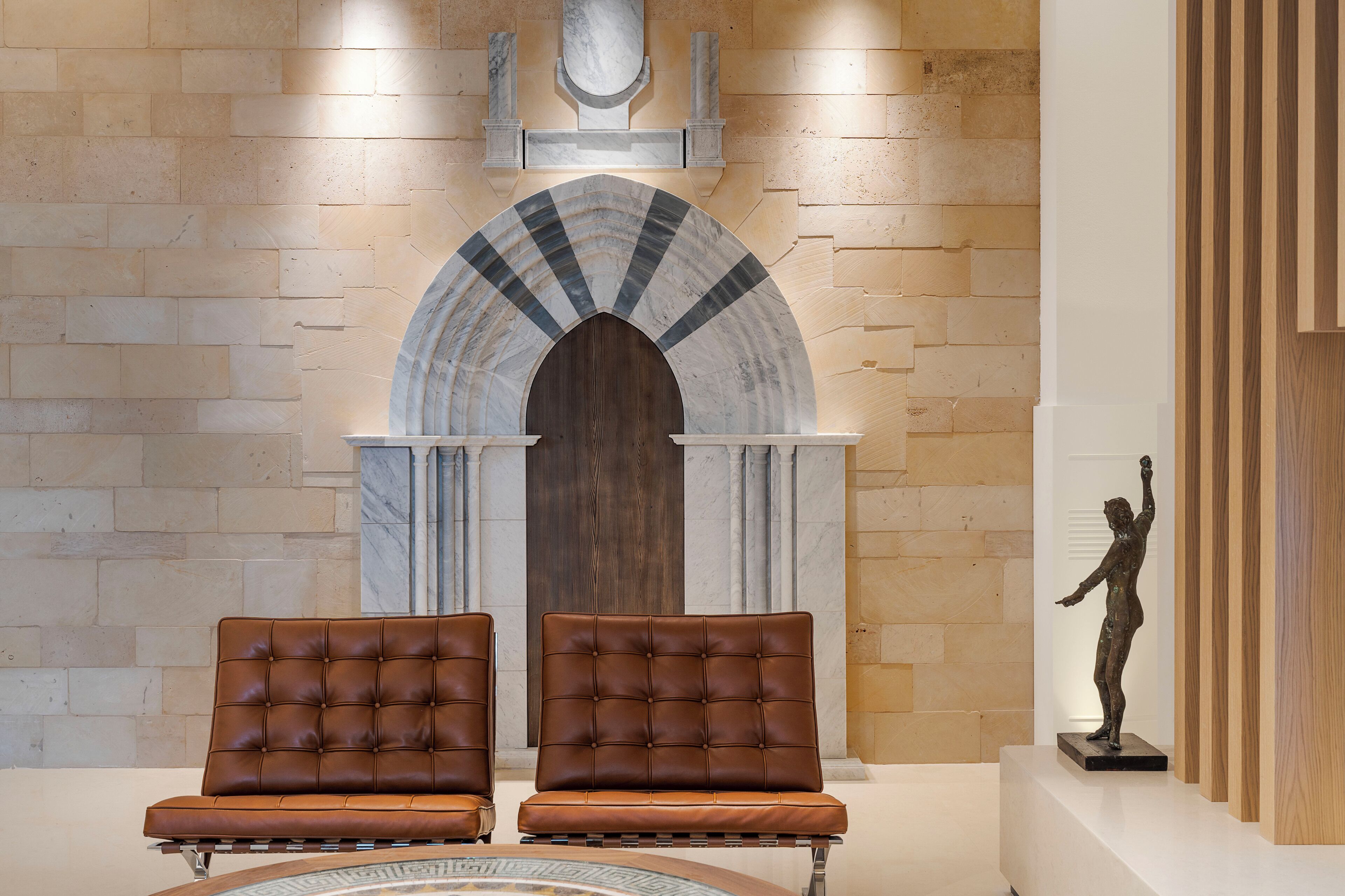 Una hall con due poltrone in pelle marrone, un arco in marmo e una statua su piedistallo.
