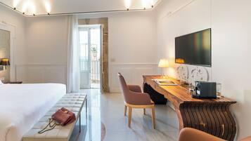 A hotel room with a bed, a bench, a desk with a chair, a TV, and a coffee machine.