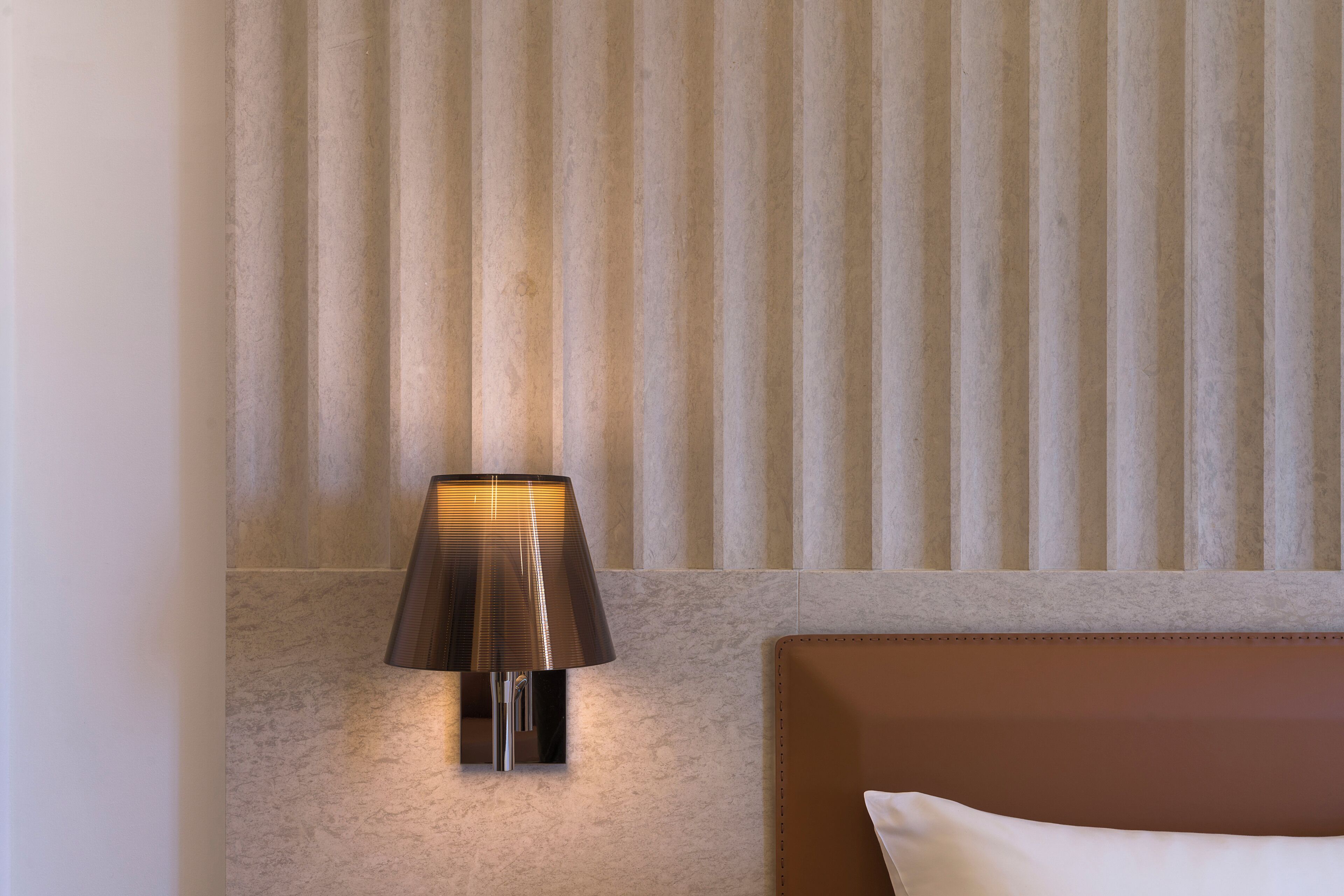 A modern room with a wall-mounted lamp, a brown headboard, and a textured wall.