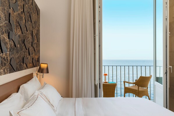 A hotel room with a bed, a view of the sea, a wicker chair, and a lamp. - Maniace Boutique Hotel Ortigia UNA Esperienze (Syracuse)