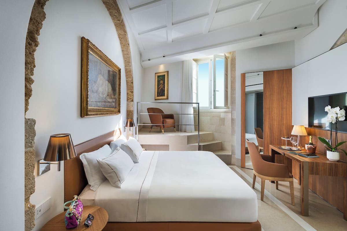 A hotel room with a large bed, a desk, a chair, a TV, and a painting on the wall.