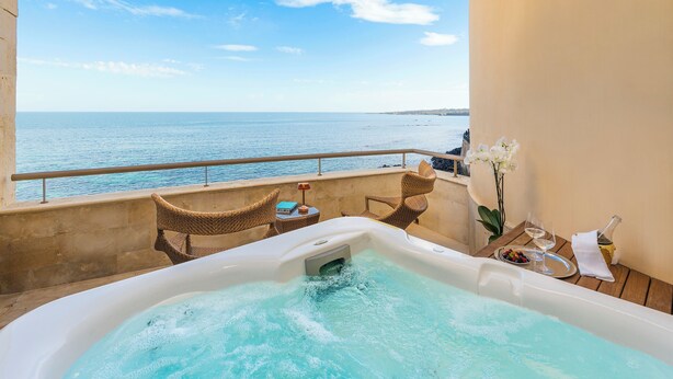 A hot tub with a view of the sea, wicker chairs, and a table with drinks and flowers. - Maniace Boutique Hotel Ortigia UNA Esperienze (Syracuse)