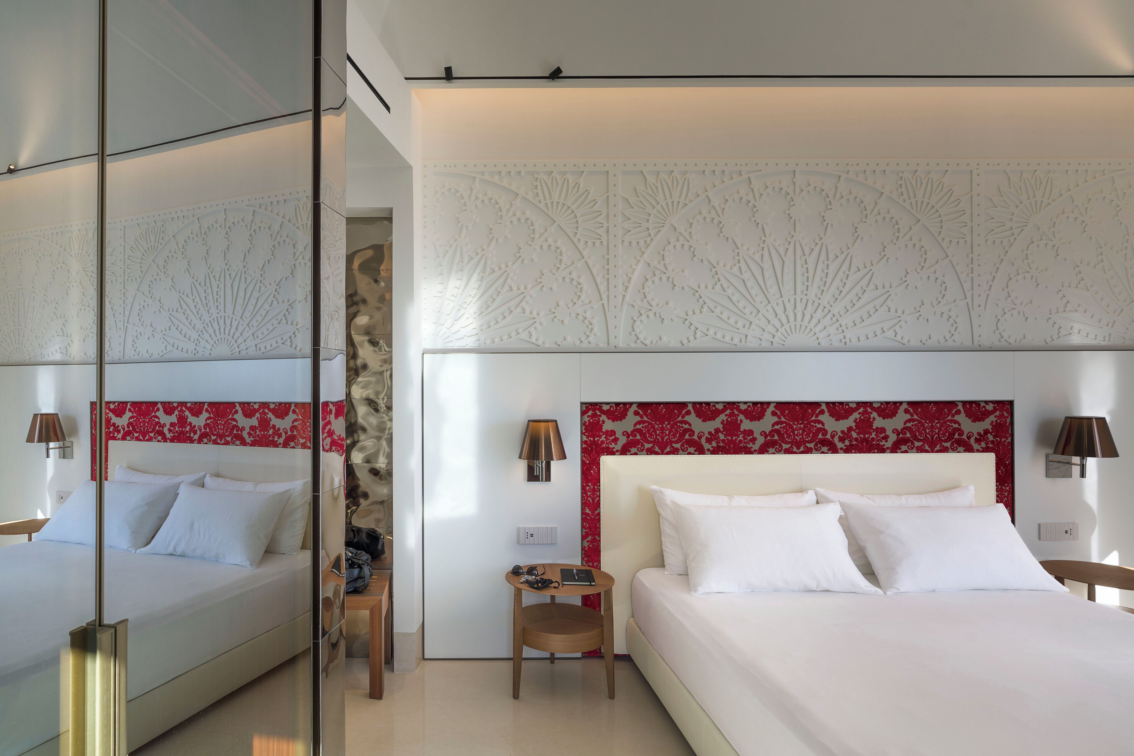 Een moderne hotelkamer met een groot bed, een klein nachtkastje, een spiegel en een decoratief hoofdbord.
