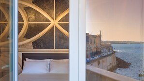 A hotel room with a large bed, a view of the waterfront, and a distinctive circular architectural feature above the bed. - Maniace Boutique Hotel Ortigia UNA Esperienze (Syracuse)