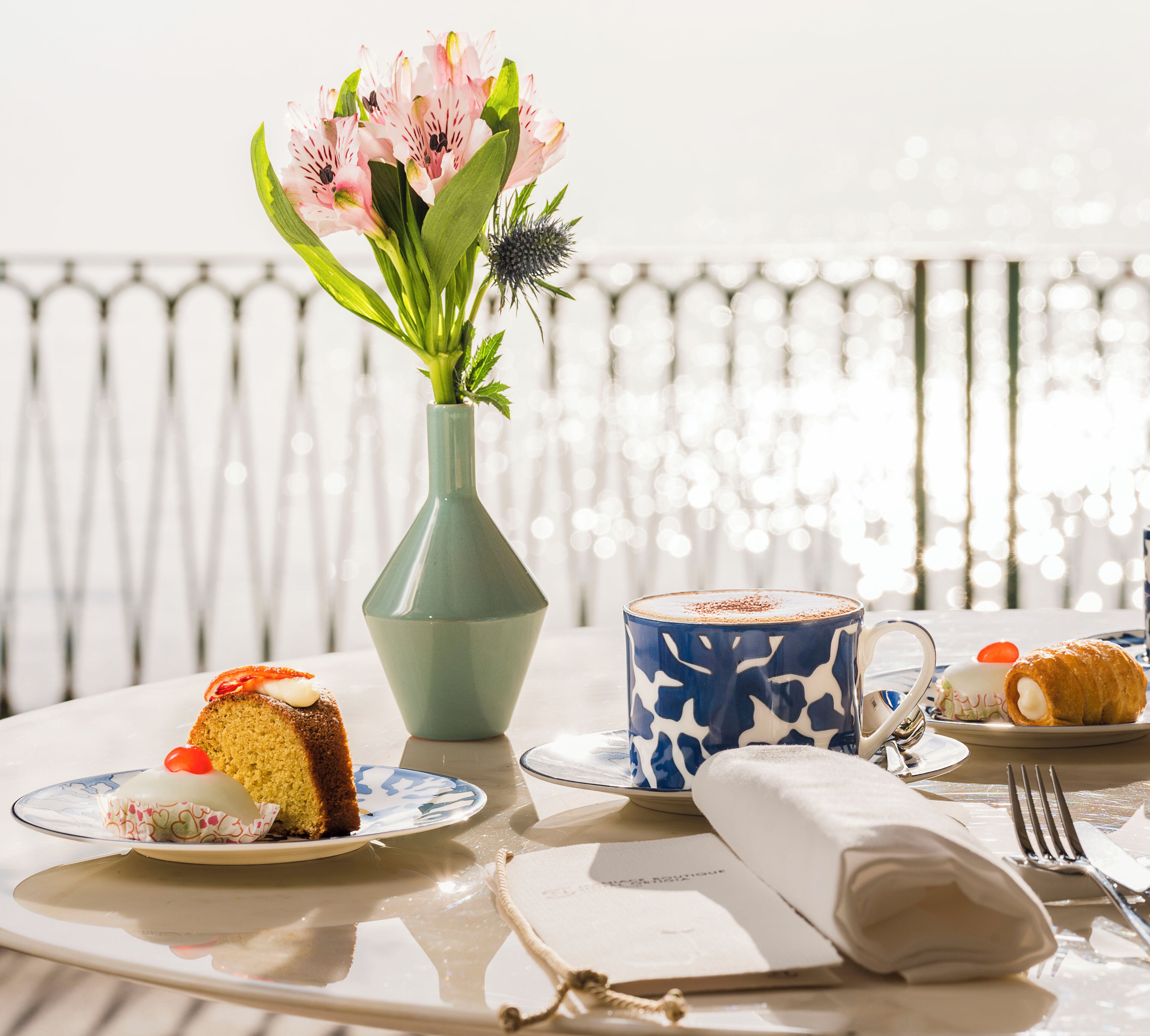 Una mesa con un pastel, una taza, un plato de comida, un florero con flores y un adorno.