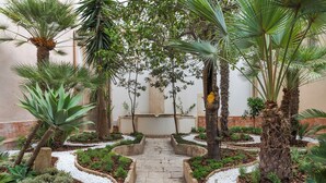 A stone pathway flanked by palm trees and small shrubs, leading to a central structure. - Maniace Boutique Hotel Ortigia UNA Esperienze (Syracuse)