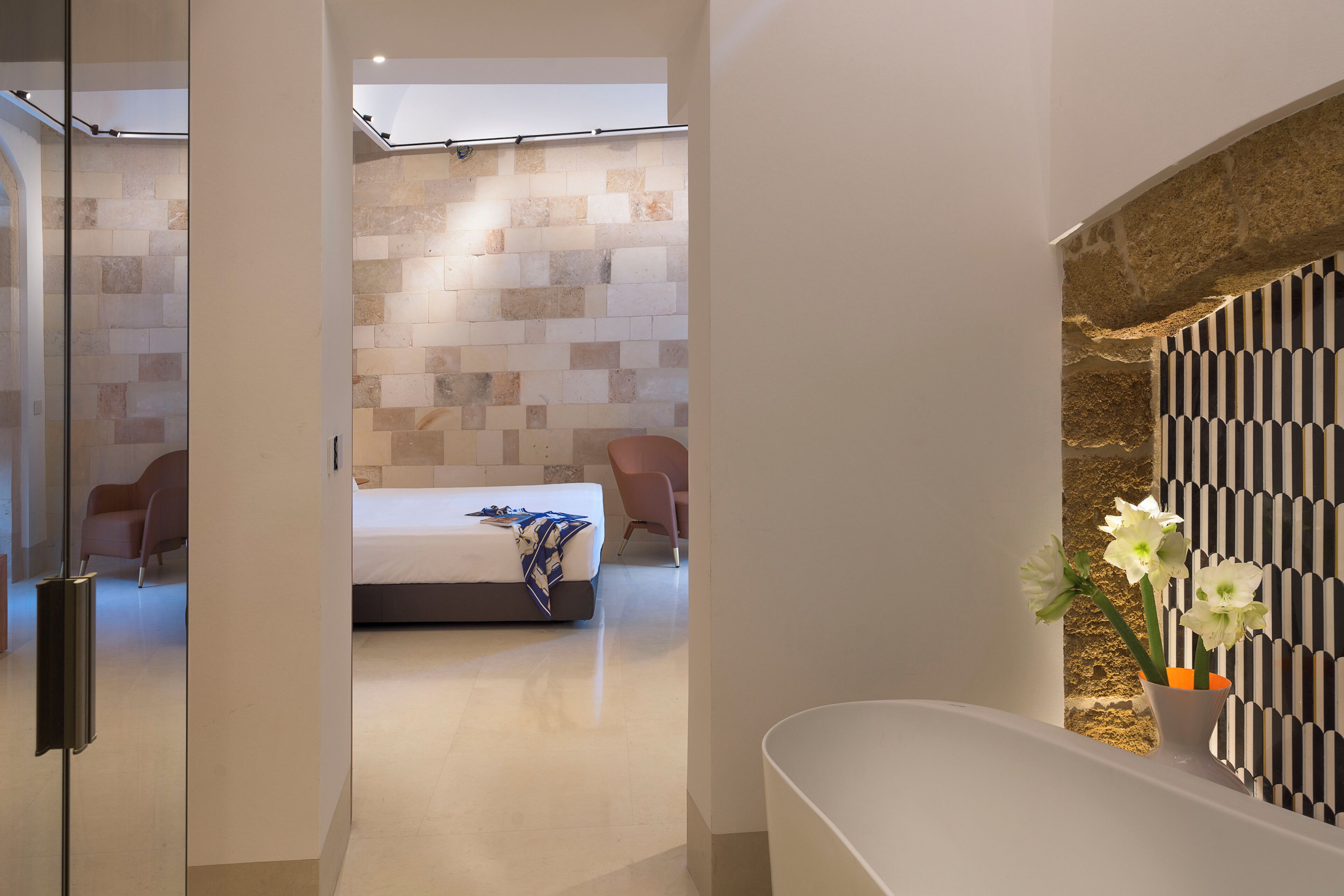 A modern hotel room with a large bed, a seating area with chairs, and a decorative wall with a geometric pattern.